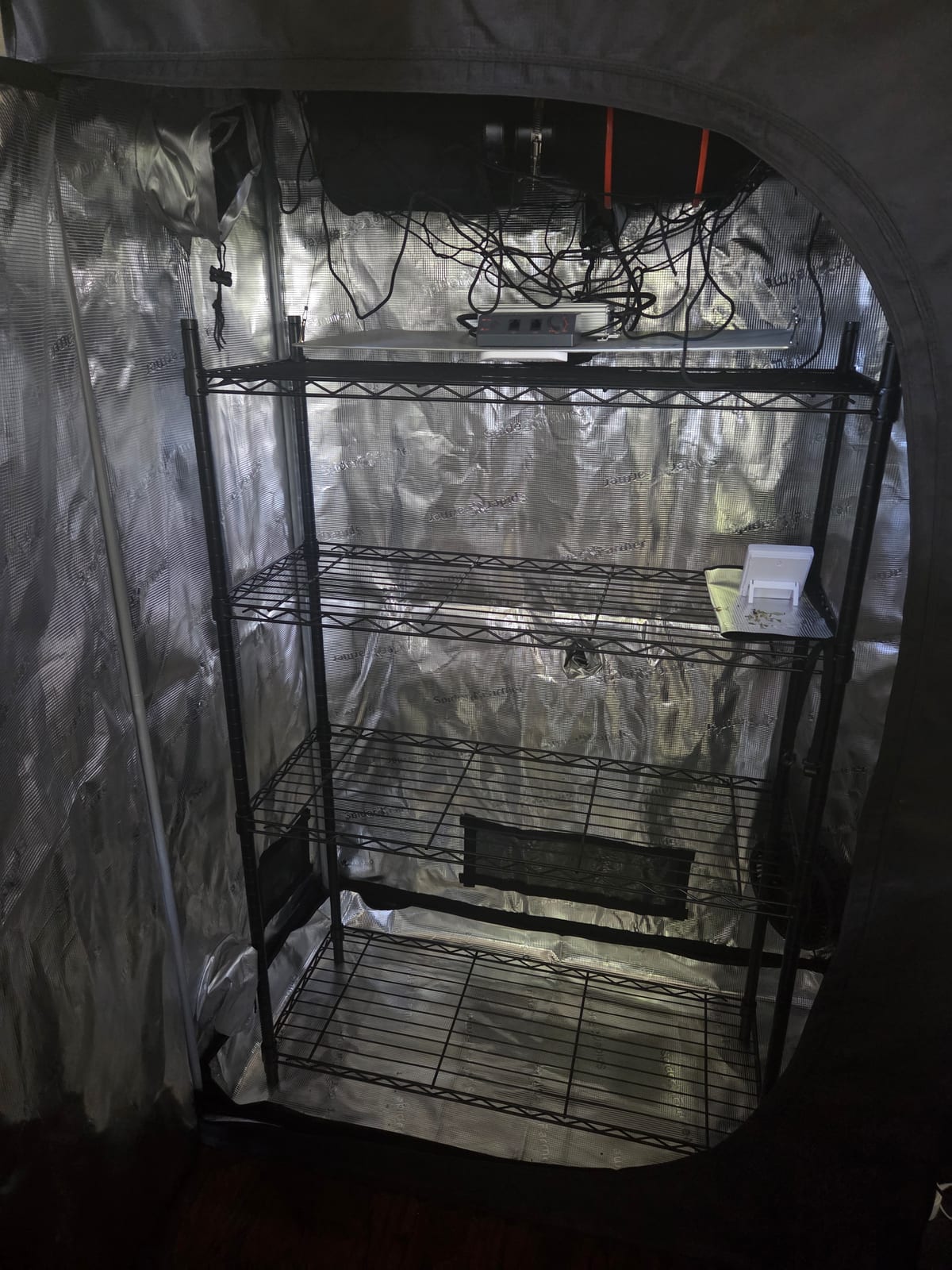 Inside the grow tent: reflective mylar walls, wire shelving racks, circulation fan and controller, still empty of plants